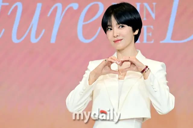 宋慧乔身穿全白短款夹克搭配高腰阔腿裤出席活动，手持麦克风发言