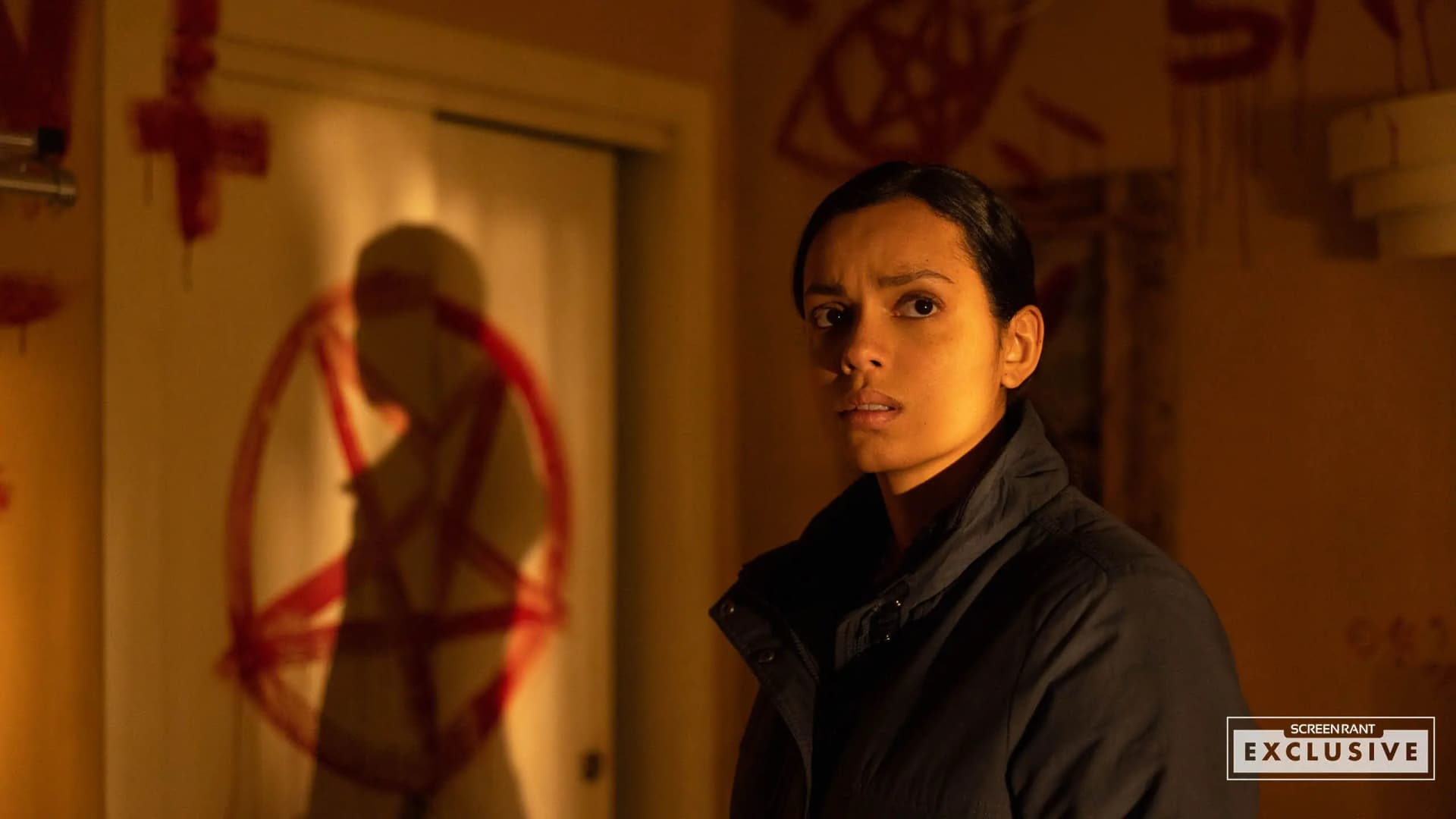 Georgina Campbell as Jane Thorne examining bloody satanic symbols and pentagrams covering a crime scene room wall in Psycho Killer